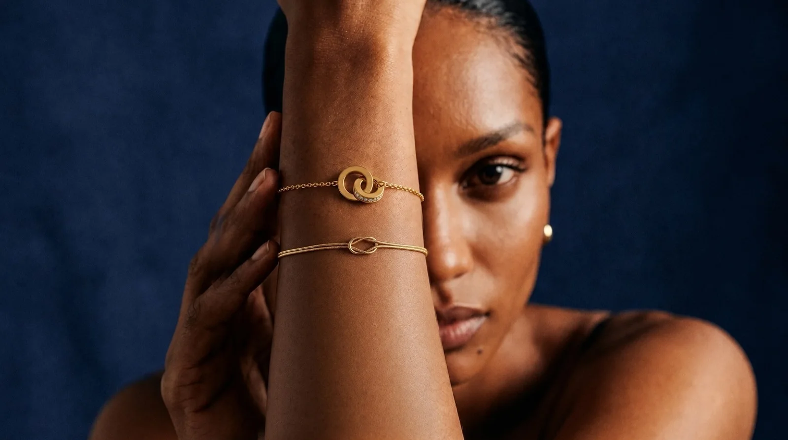 A woman under a shower with her eyes closed, water running over gold-plated hoop earrings, a fine chain and a ring